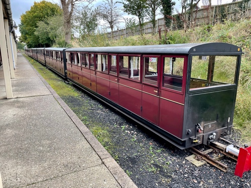 A row of burgundy carriages, with the interiors more clearly visible -- there are five doors on each carriage, leading to a compartment with bench seats facing each other.